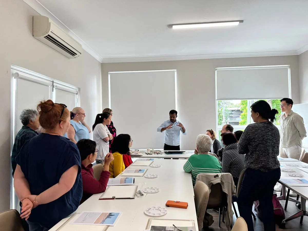 Arafat Hosen speaking to participants gathered around tables set with paper, palettes and reference prints